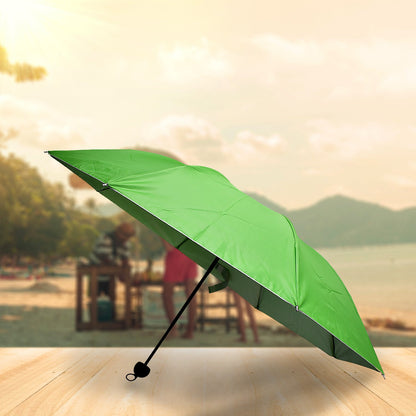A green umbrella with a black handle is open on a wooden surface, with a blurry beach scene in the background.