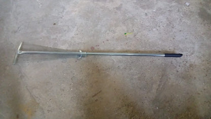 A gardener using the versatile garden rake to smooth soil in a neatly maintained yard.