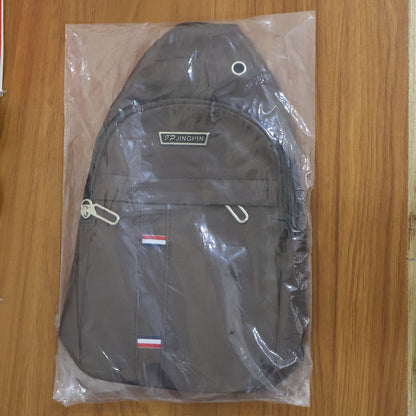 A brown leather sling bag is sealed inside a clear plastic bag, showcasing its front pockets and strap.
